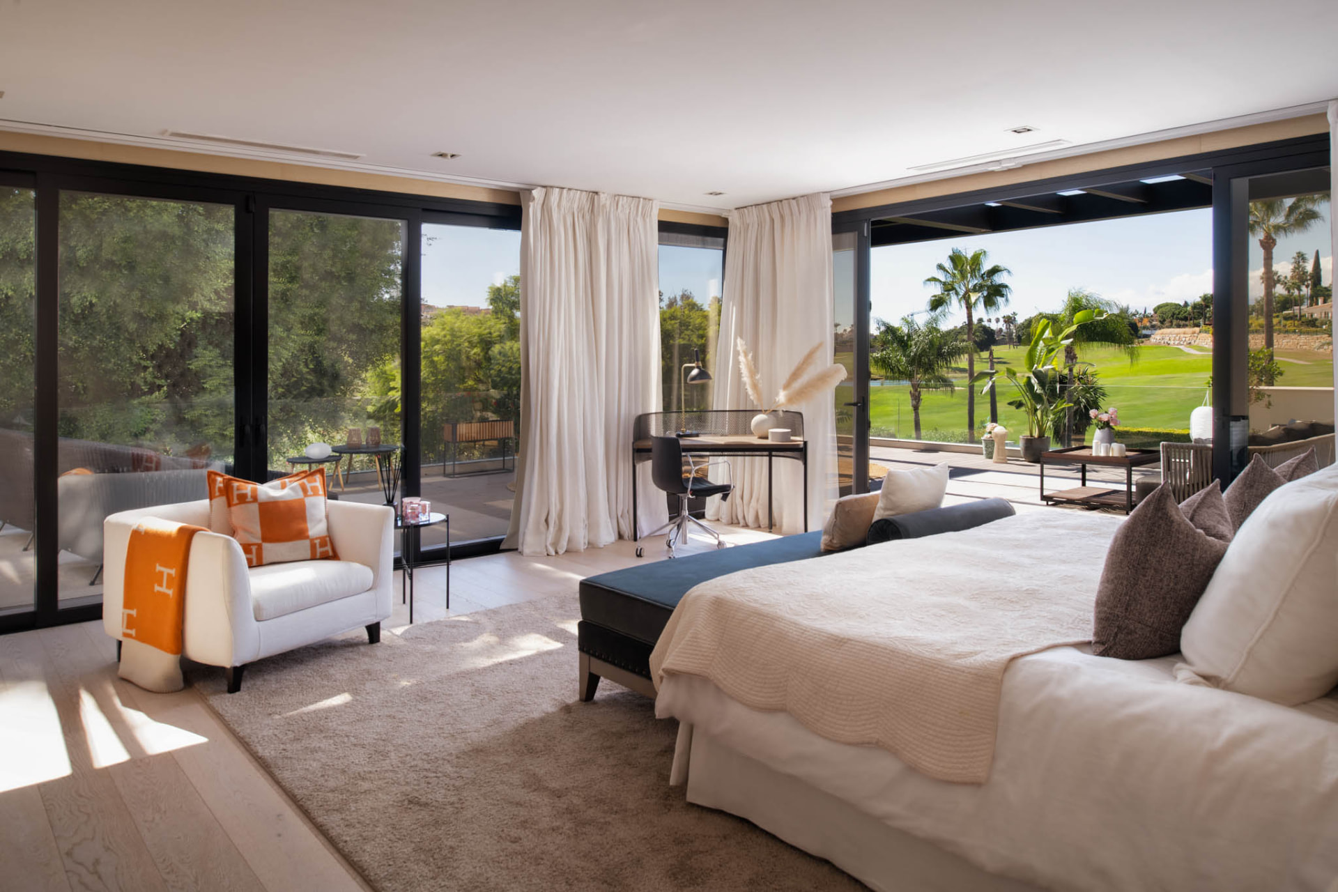 An upper-floor bedroom with wide glazing opening onto a terrace overlooking the golf landscape.